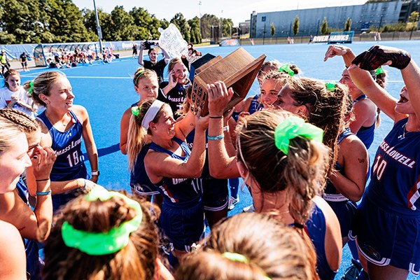 College field hockey players celebrate a win by hoisting a trophy on the field