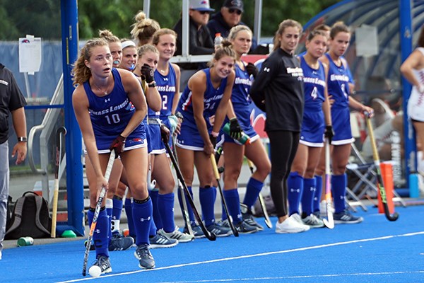 A field hockey player looks to pass while teammates watch from the sideline
