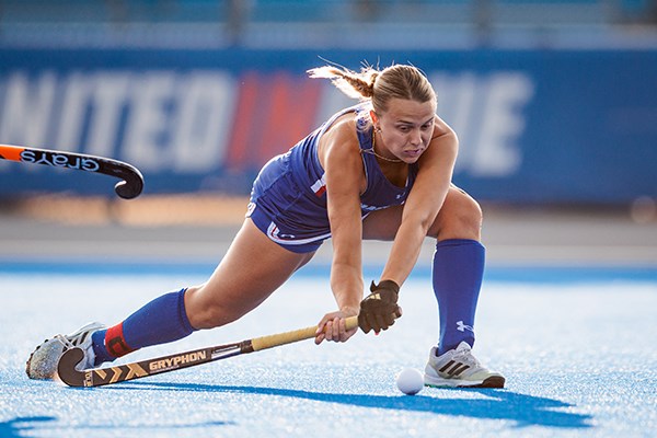 A field hockey player lunges for a shot on a blue turf field
