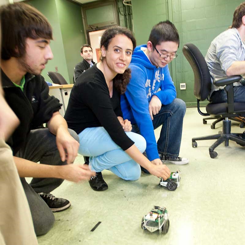 Student works with a robot while others watch in a UMass Lowell electrical and computer engineering classroom