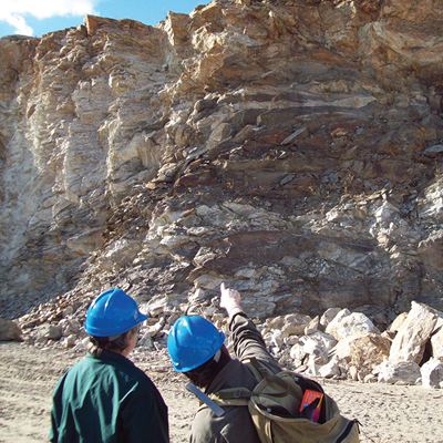 Two people with hard hats pointing at a rocky cliff