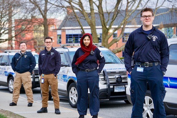 Four student EMTs stand by their vehicles on East Campus