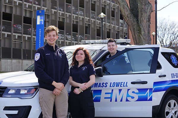 Three student EMTs pose for a photo with their emergency vehicle