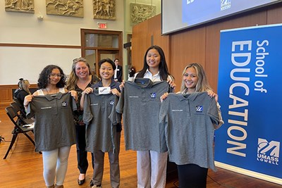 Four Lowell High School students who plan to become teachers hold up UMass Lowell School of Education polo shirts at UML's fall 2022 education symposium