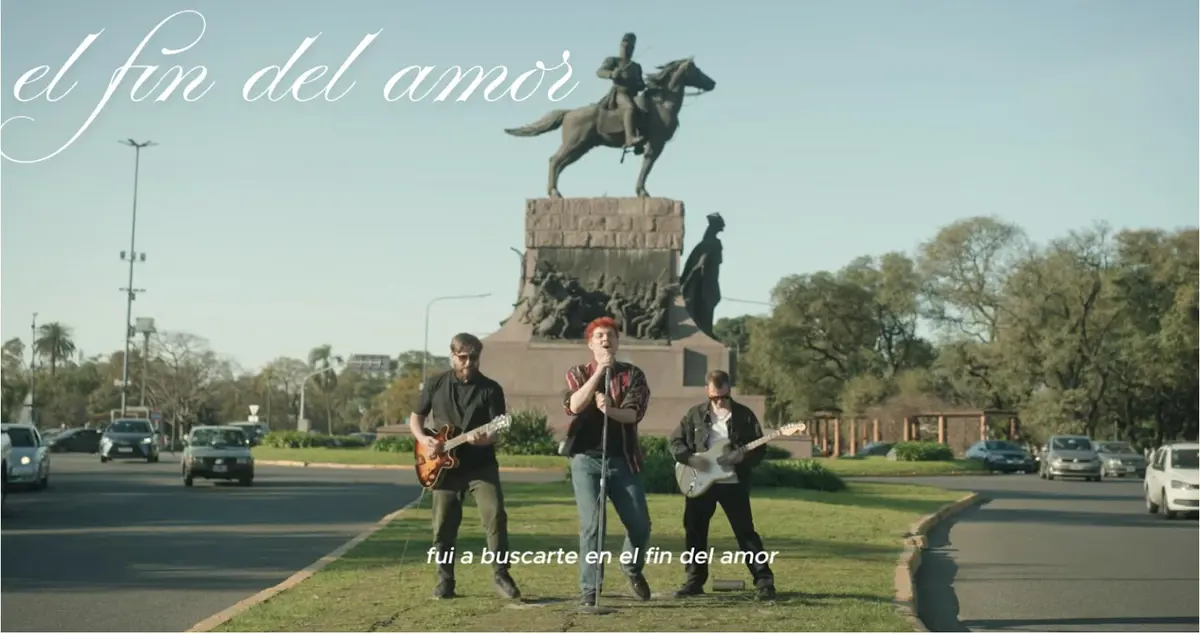 A singer and 2 guitarists perform in an intersection. Text reads: "el fin del amor" and “fui a buscarte en el fin del amor”.