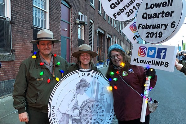 Lowell National Historical Park supervisory park ranger David Byers, ranger Emma Mitchell, and UMass Lowell's Ellen Anstey promote the new Lowell quarter at the city's 2018 Festival of Lights