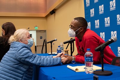 Sean Ellis holds the hands of an older woman across a table while speaking to her after a panel at UMass Lowell 
