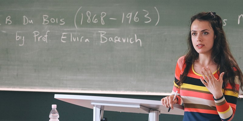 Asst. Prof. Elvira Basevich in front of a blackboard with her name written on it.