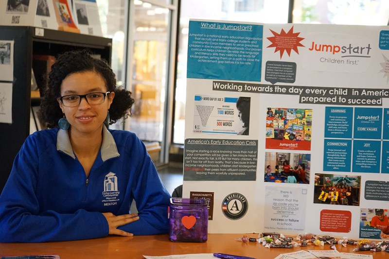 Emily Crespo sits at a table with a Jumpstart poster.