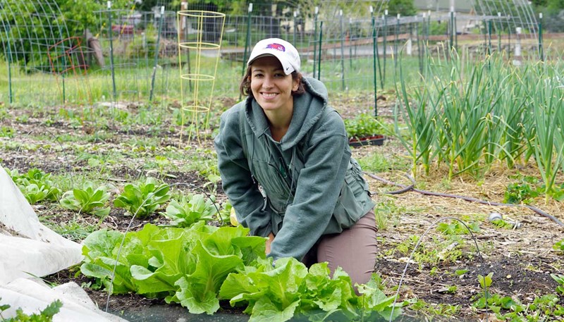 Emily Makrez poses next to lettuce growing on her farm.