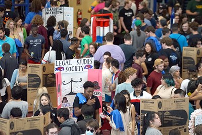 Students mill around displays for student organizations inside a gym