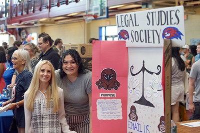 Two women pose for a photo next to a display for the Legal Studies Society