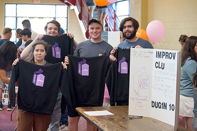 Four students hold up black shirts that say Improv UML and pose for a photo