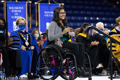 A woman in a wheelchair holds a microphone while speaking on stage