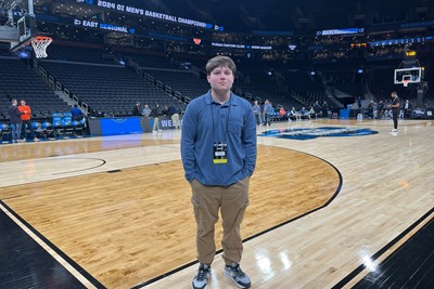 A person poses for a photo while standing on the corner of a basketball court in an arena.