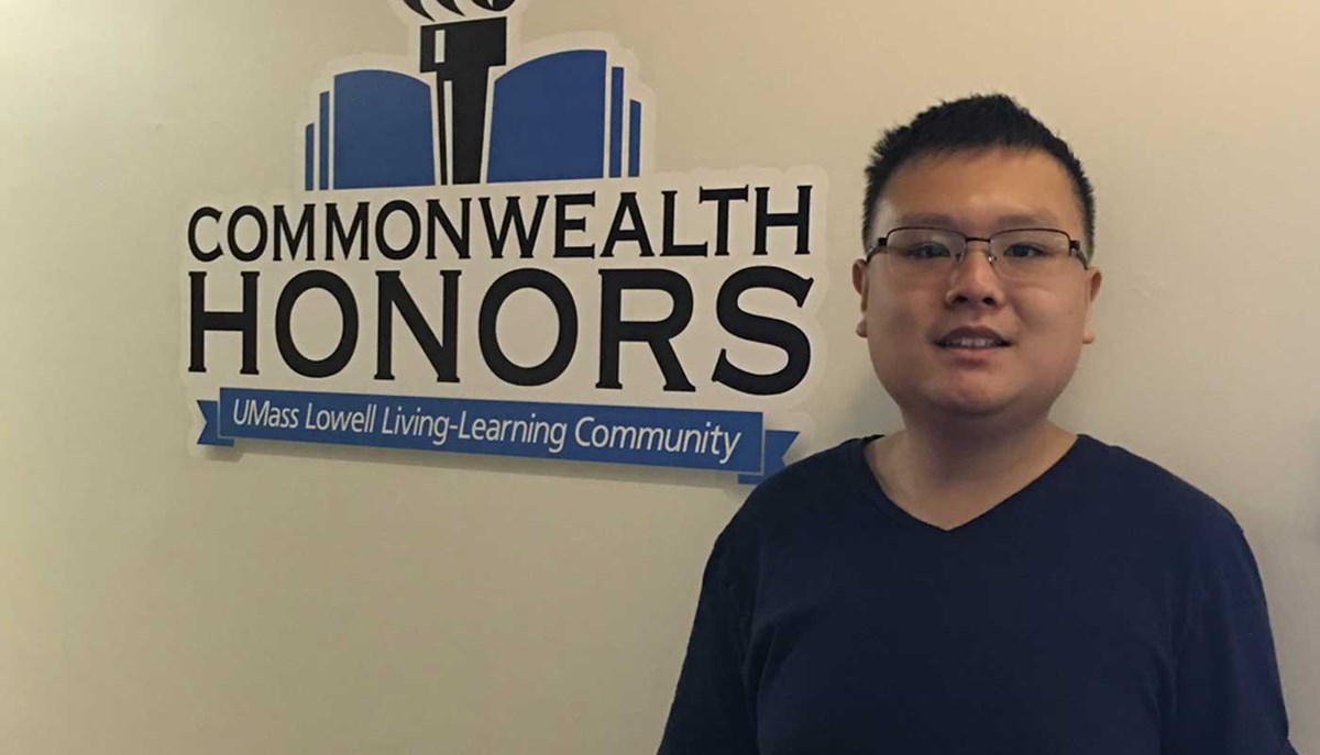Plastics engineering student Evan Yu poses in front of a sign with "Commonwealth Honors: UMass Lowell Living-Learning Community"