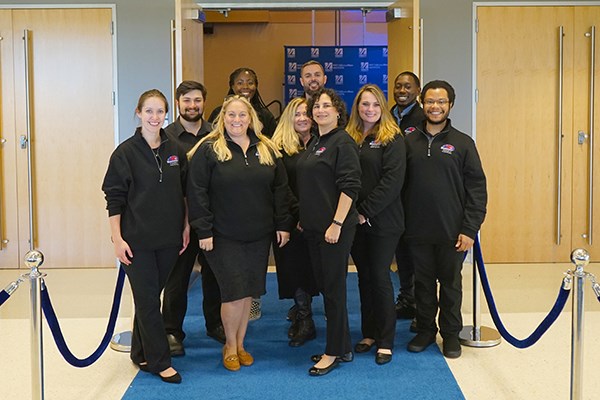Ten members of the Event Services team pose for a photo in a doorway at UCrossing
