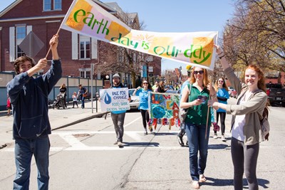 People celebrating Earth Day in the sunny streets of Lowell while holding up a banner that reads "Earth Day is Our Day".