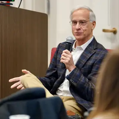 A business executive speaks to an audience while holding a microphone.