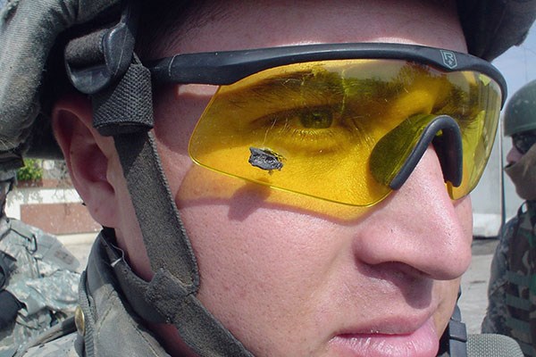 A soldier wearing yellow tinted protective glasses with a piece if shrapnel stuck in the lens.