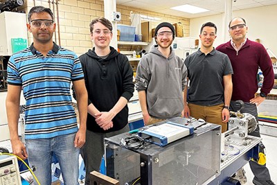 Team of researchers standing behind the helium-powered gas gun that tests materials.