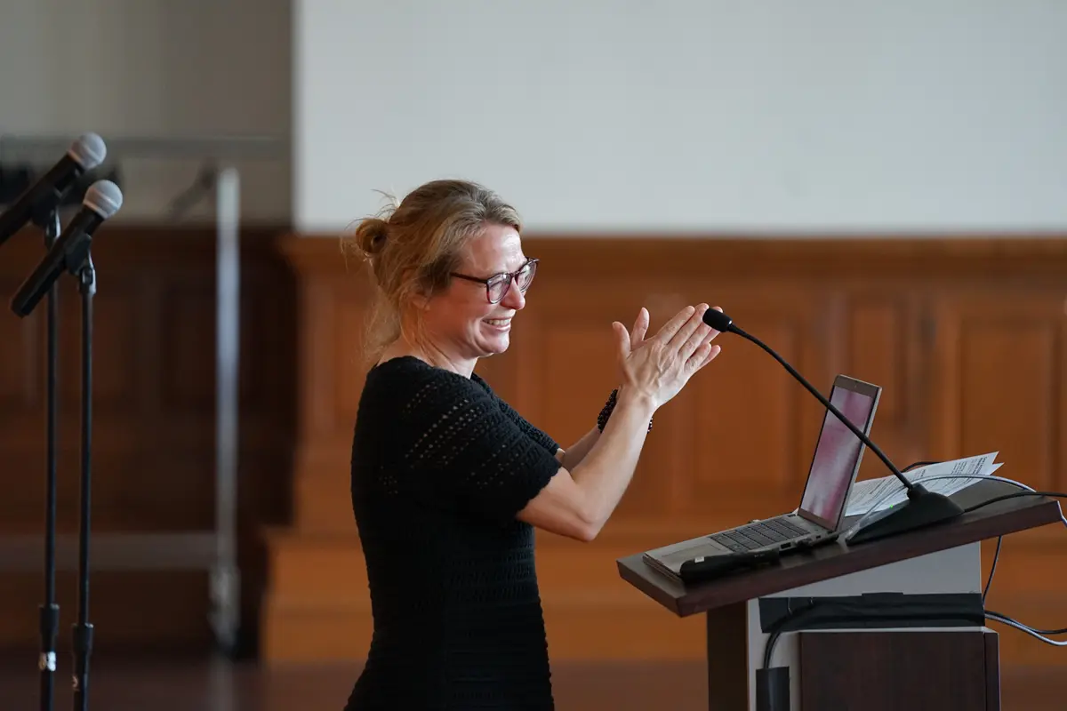 French Associate Professor Mercedes Baillargeon stands before a podium and microphone at a campus celebration