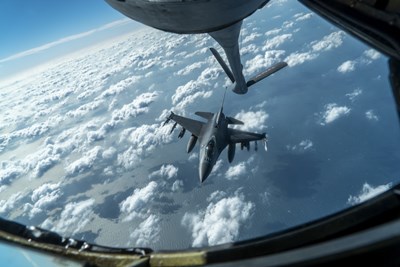 F-16 Fighting Falcon flying below aerial refueling boom arm.