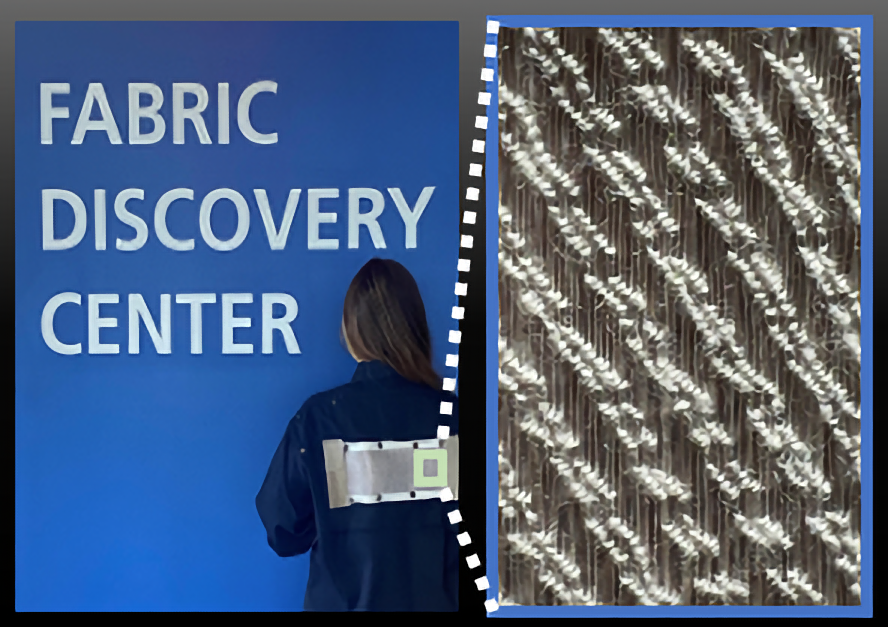 Person in-front of blue background with: Fabric Discovery Center. Zoom in back of coat shows HEROES solar fabric research project on right.