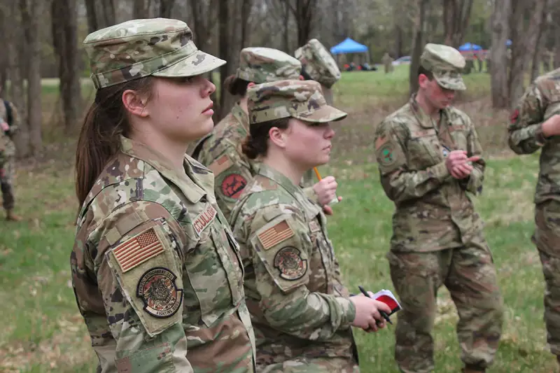 Cadets in fatigues stand in a field with small notebooks.