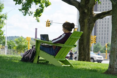 A student uses their laptop outside while seating in a green Adirondack chair