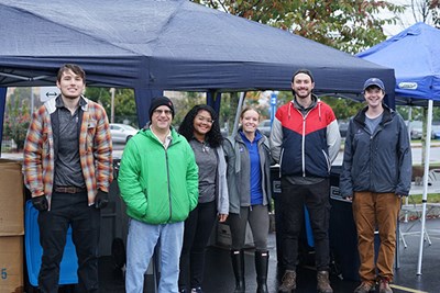 A group of six people pose for a photo while standing in front of two blue tents