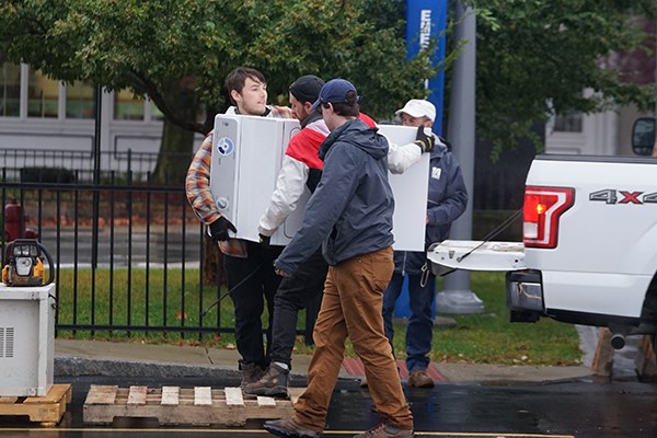 Two students unload a white washing machine from the back of a white pickup
