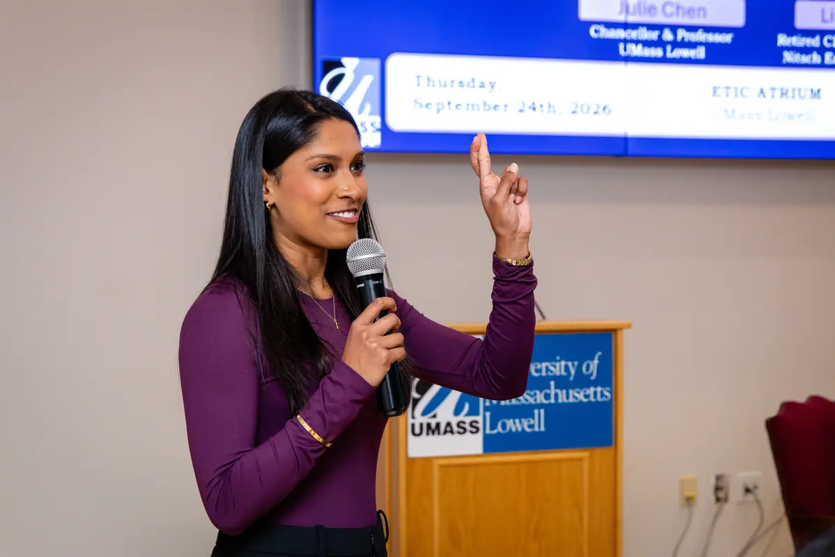 A young woman with dark hair crosses her fingers while speaking into a microphone.