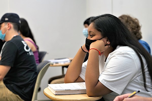 A female student with dark hair wearing a face mask listens in class 