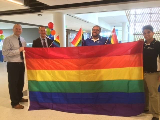 Four men standing and holding up rainbow Pride flag