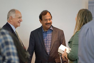 Two men in suit jackets smile while talking to a woman