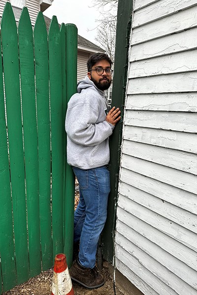 UML business major Rohan Solanki demonstrates how he squeezed between his fraternity's garage and the backyard fence to help rescue neighbors from a burning house