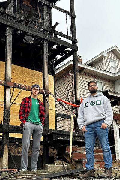 UML fraternity members Arseniy Ohorilko, left, and Rohan Solanki stand in front of the burned house and the melted vinyl on a house next door.