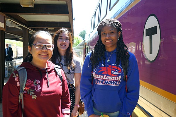 Three students stand outside a commuter rail train in Lowell