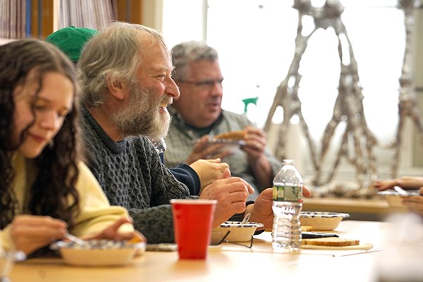 A man with a beard smiles while eating soup at a table