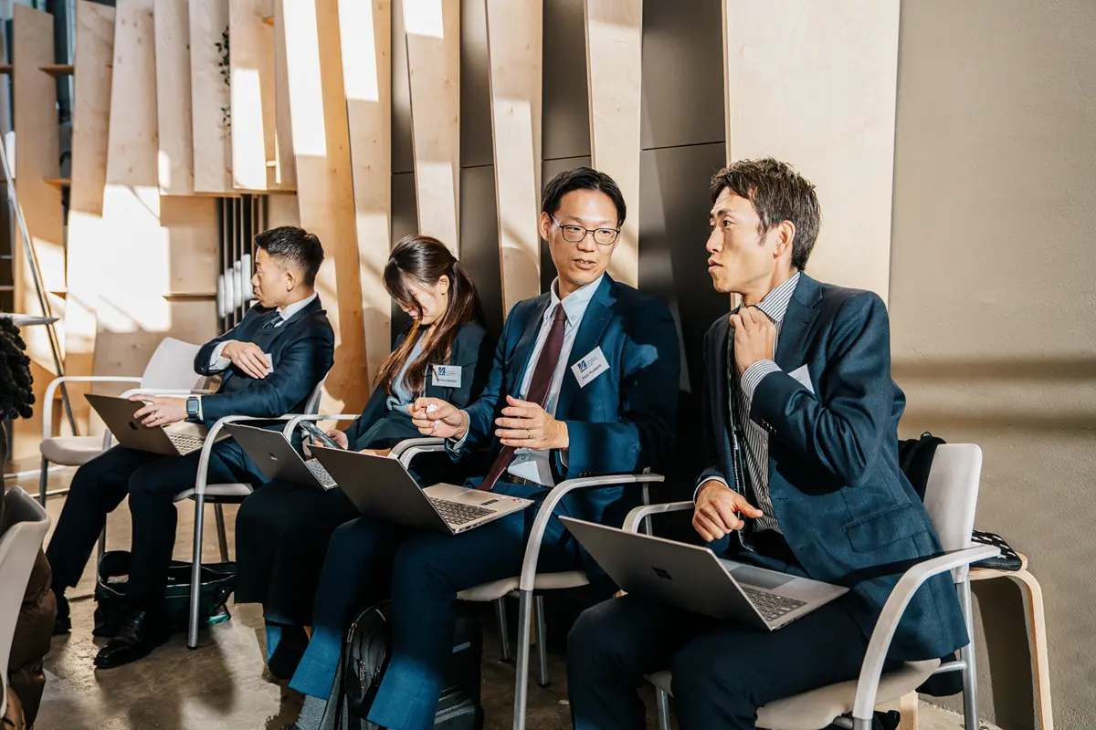 Three men and a woman in business attire sit with laptops in chairs.