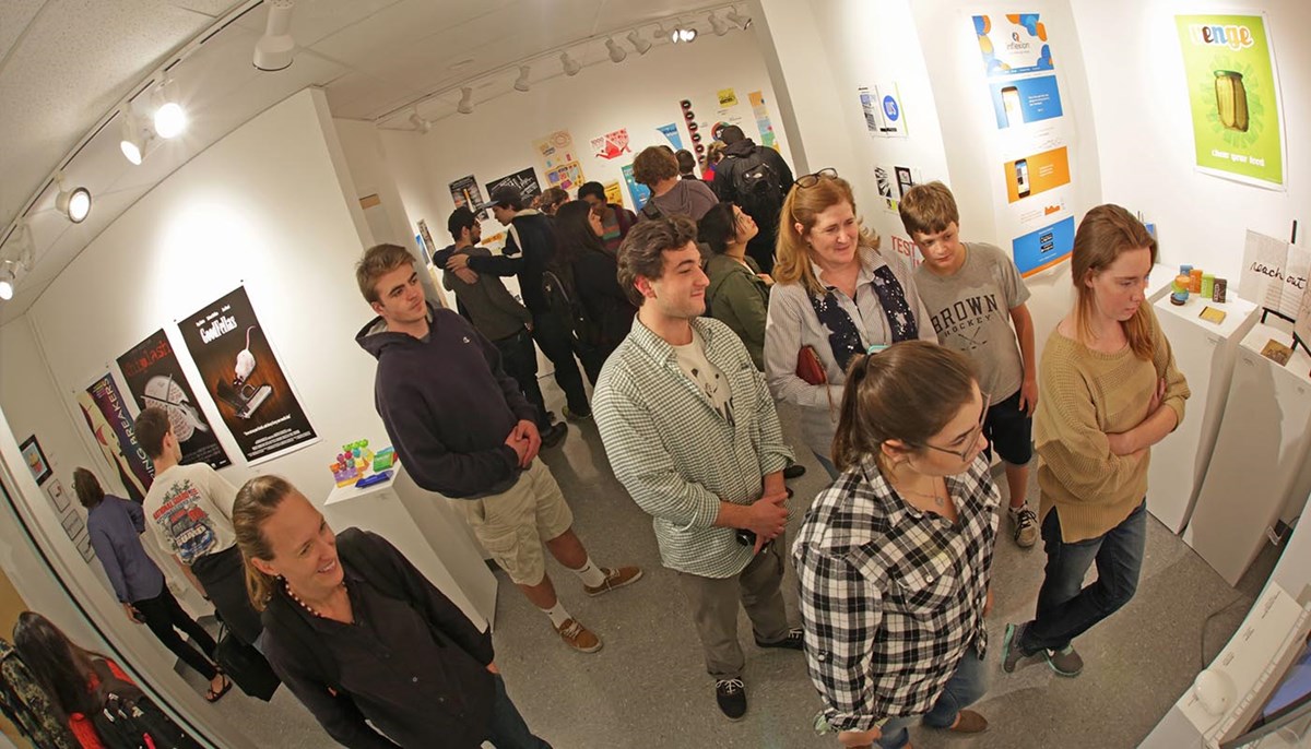 A large group of students and professors looking at artwork from a gallery at UML's Graphic Design Show. 