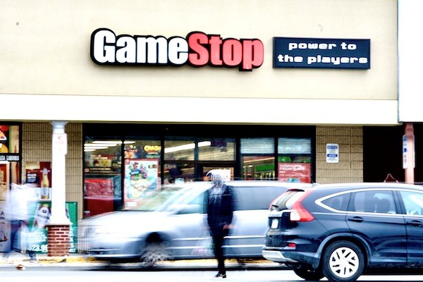 Cars and people in a parking lot in front of a GameStop store