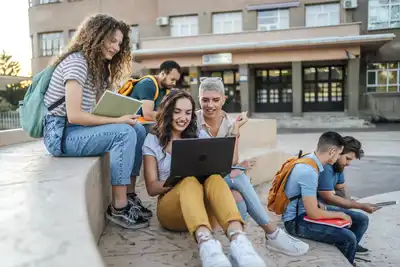 oup of students sitting outdoors, hanging out, talking and using laptop.