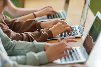 Three sets of hands all typing on laptops,