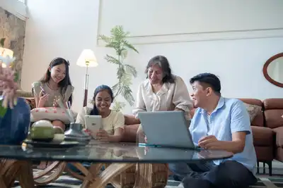 Four people gather around digital devices in a living room, collaborating around a coffee table.