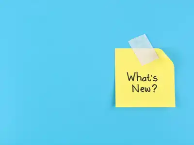 What's New text handwritten on yellow adhesive note taped on blue background .