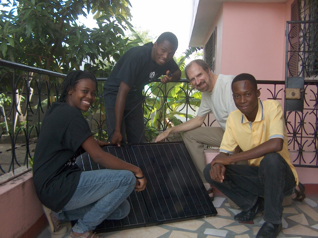 UMass Lowell Professor, Bob Giles poses with three Haitian teens while holding solar panels.
