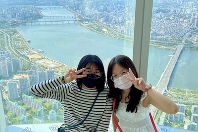 Two women make peace signs with their hands while posing for a photo high above a city