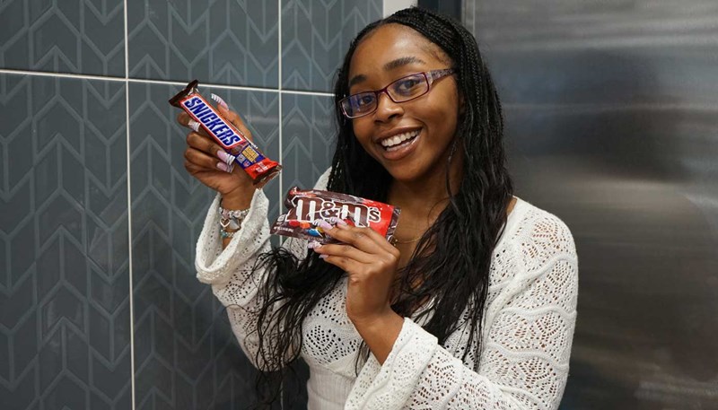 UMass Lowell student Ginika Okoli smiles while holding two candy bars.